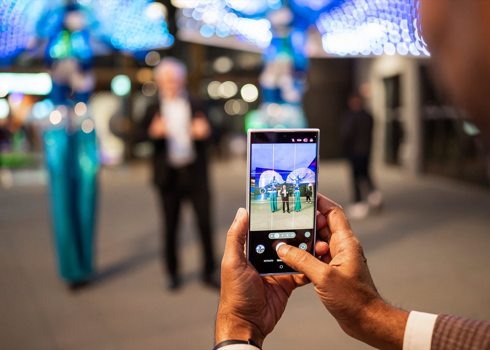 Attendee photographing costumed stilt performers on a phone