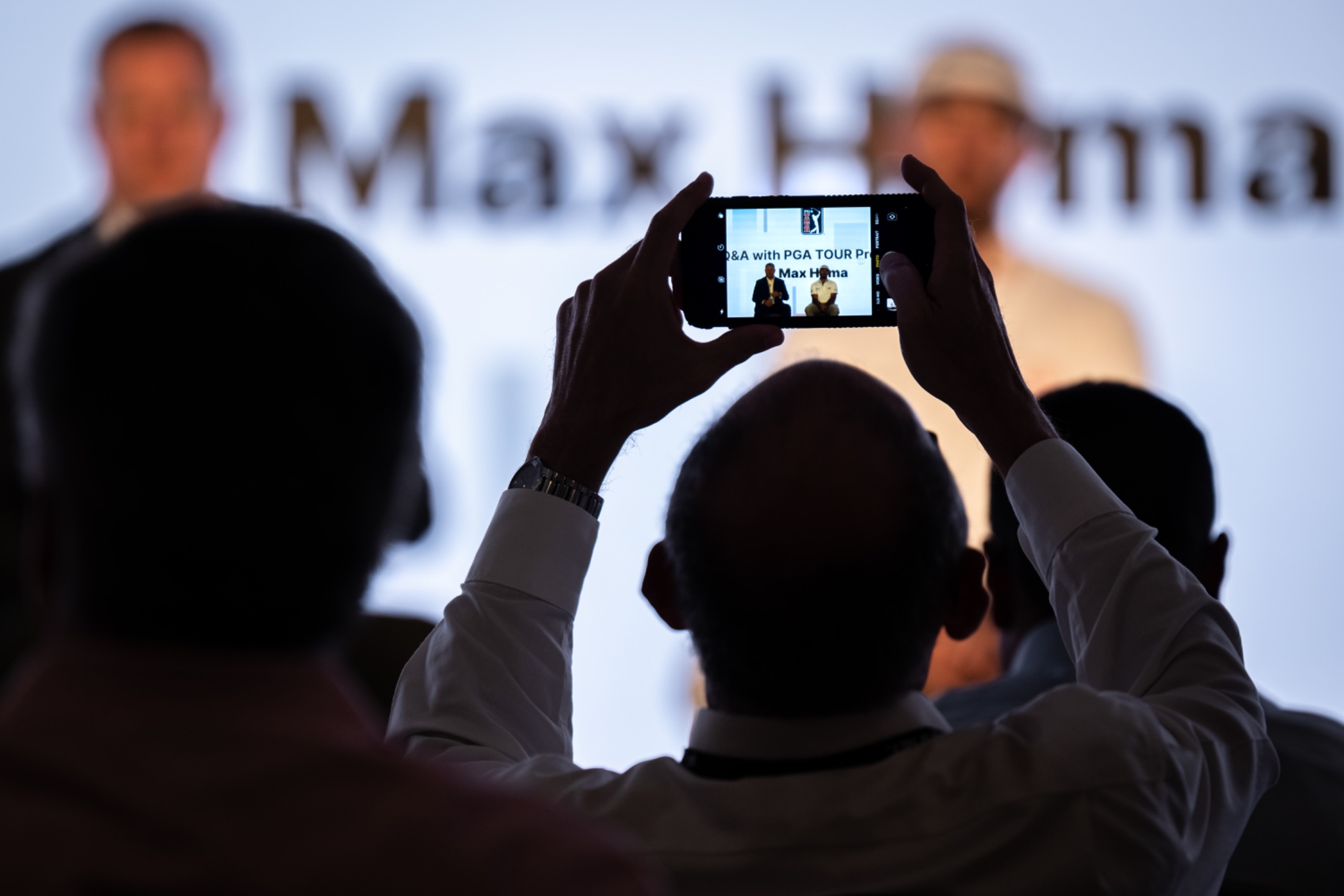 Audience member holding up a phone to photograph a live Q&A