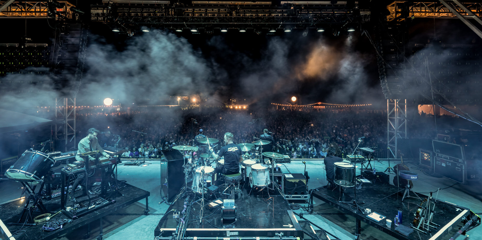 View from behind the drum kit over the crowd in blue stage haze