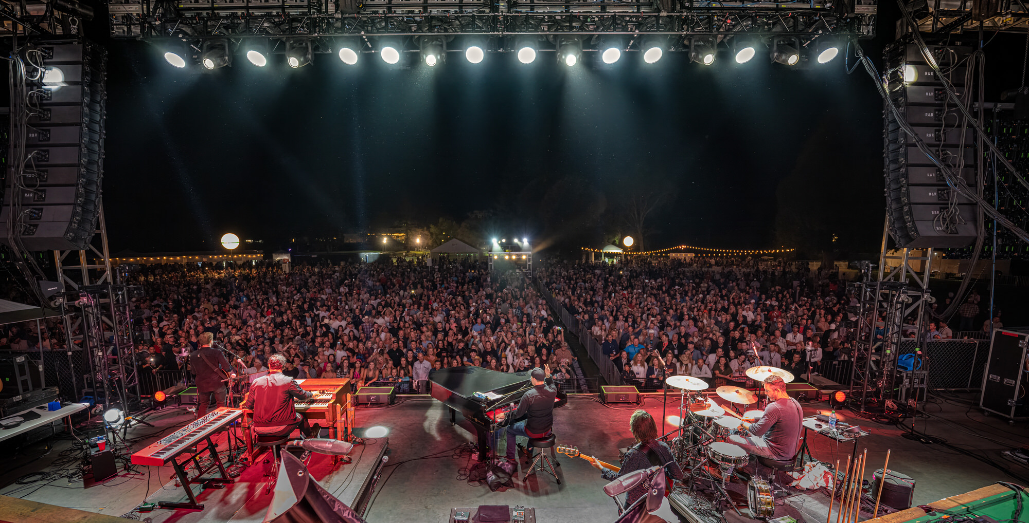 Band playing to a packed outdoor crowd, seen from the back of the stage