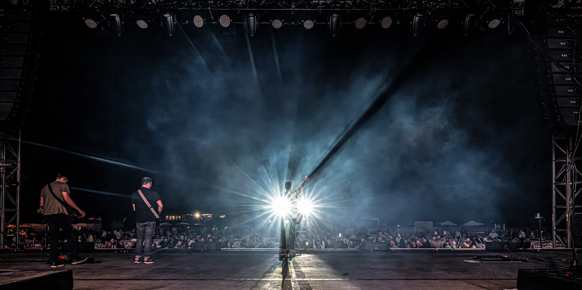Musicians silhouetted by a spotlight beam cutting through stage haze