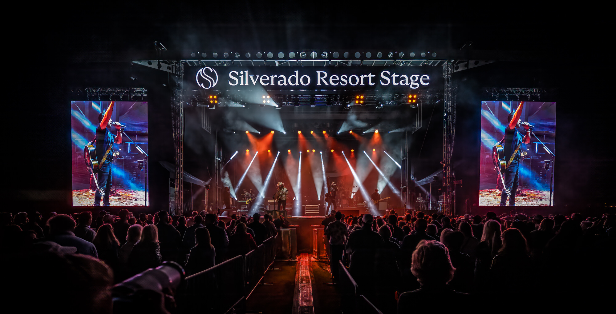 Outdoor concert stage with side screens and red lights over the crowd