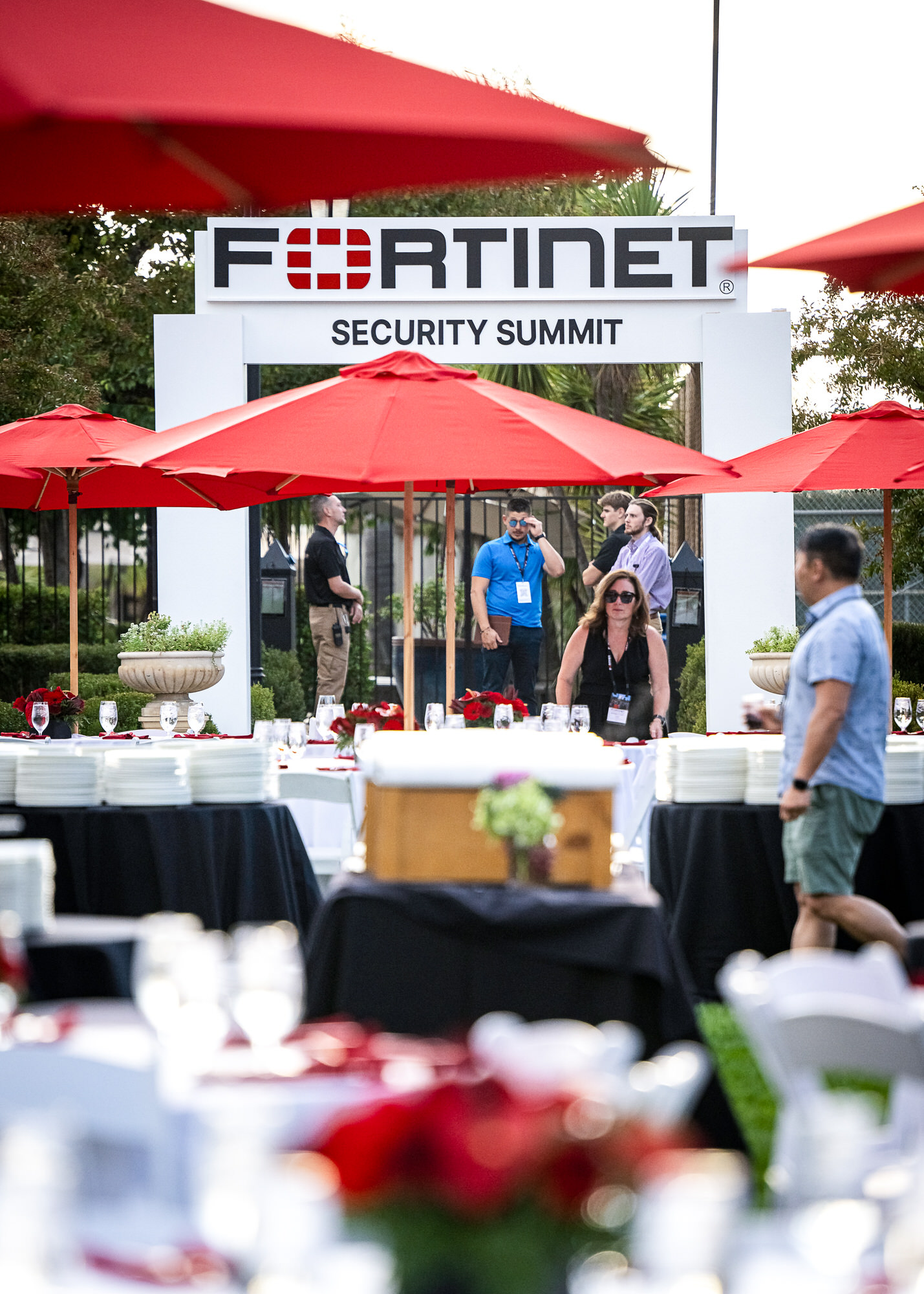 Branded entrance arch leading into an outdoor reception with red umbrellas