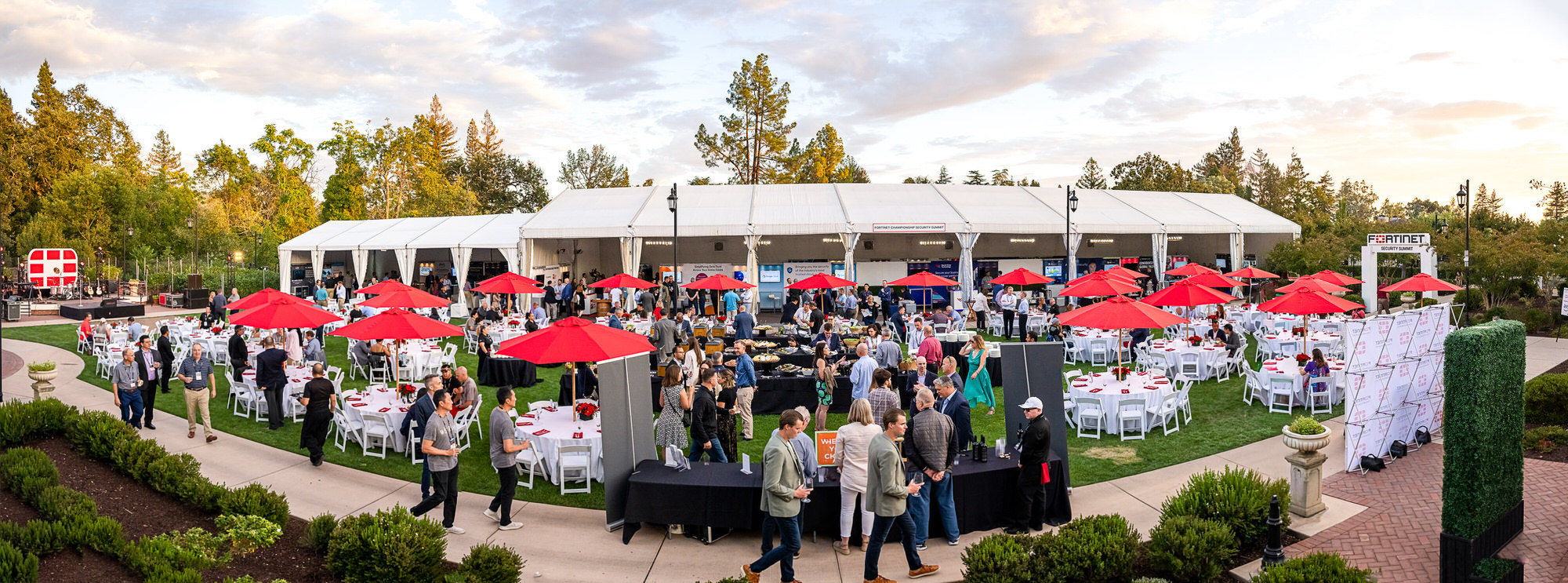 Guests mingling at an outdoor evening reception with white tents and red umbrellas