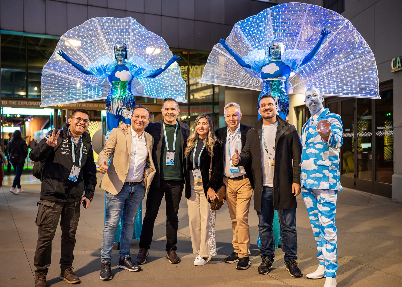Attendees posing with stilt performers in lighted costumes at an evening event