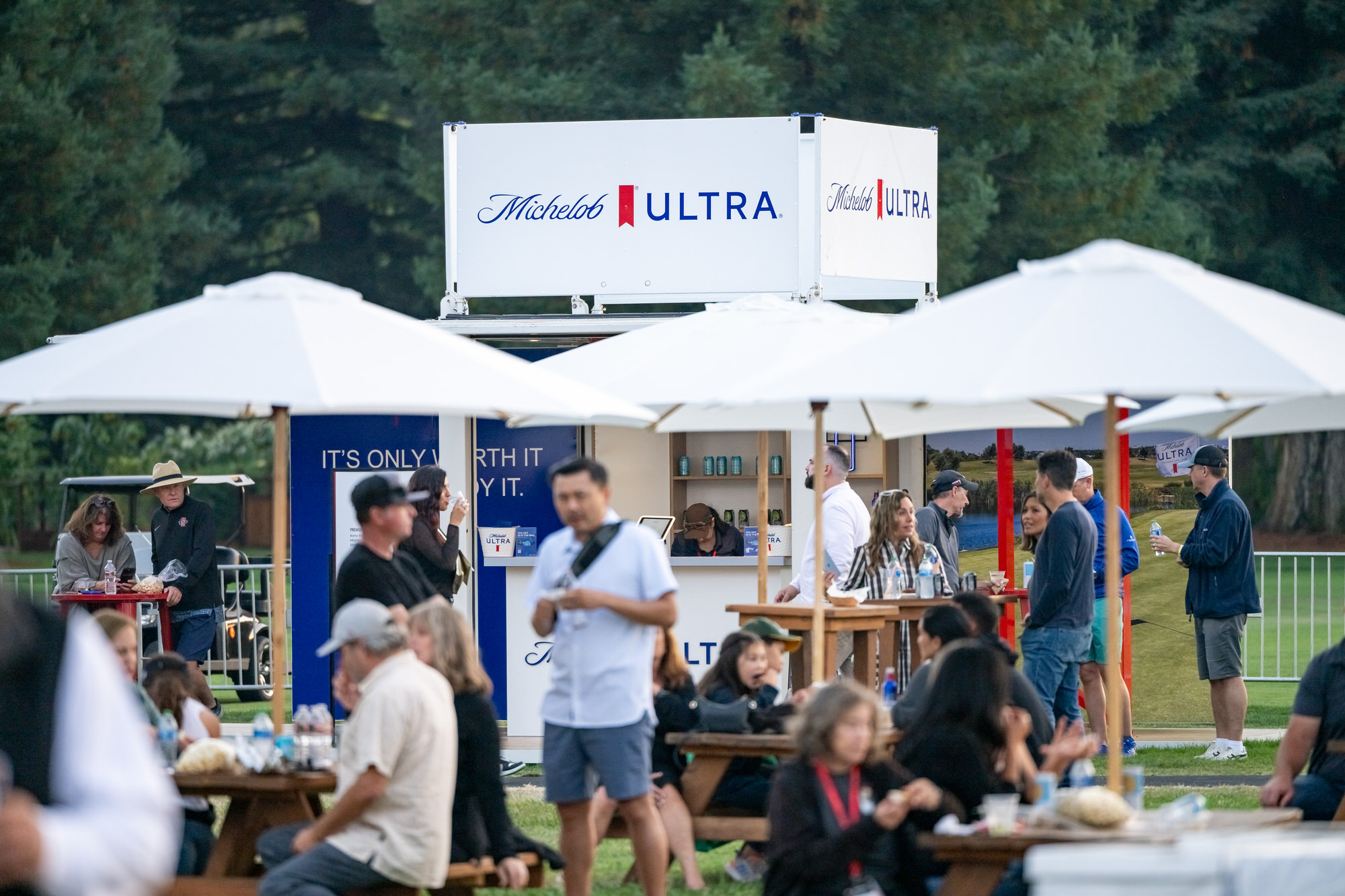Guests eating at picnic tables under white umbrellas in a hospitality area
