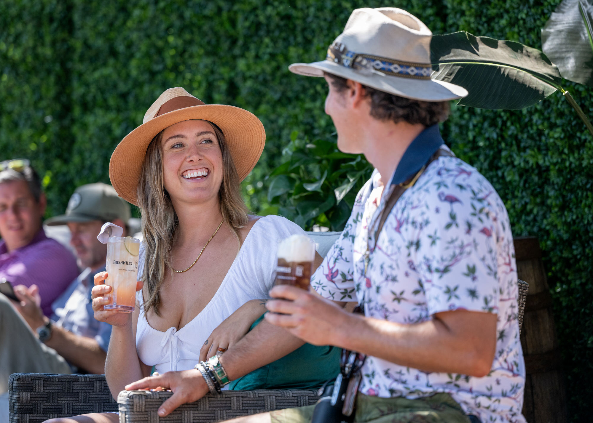 Two guests in sun hats laughing over drinks in a hospitality lounge