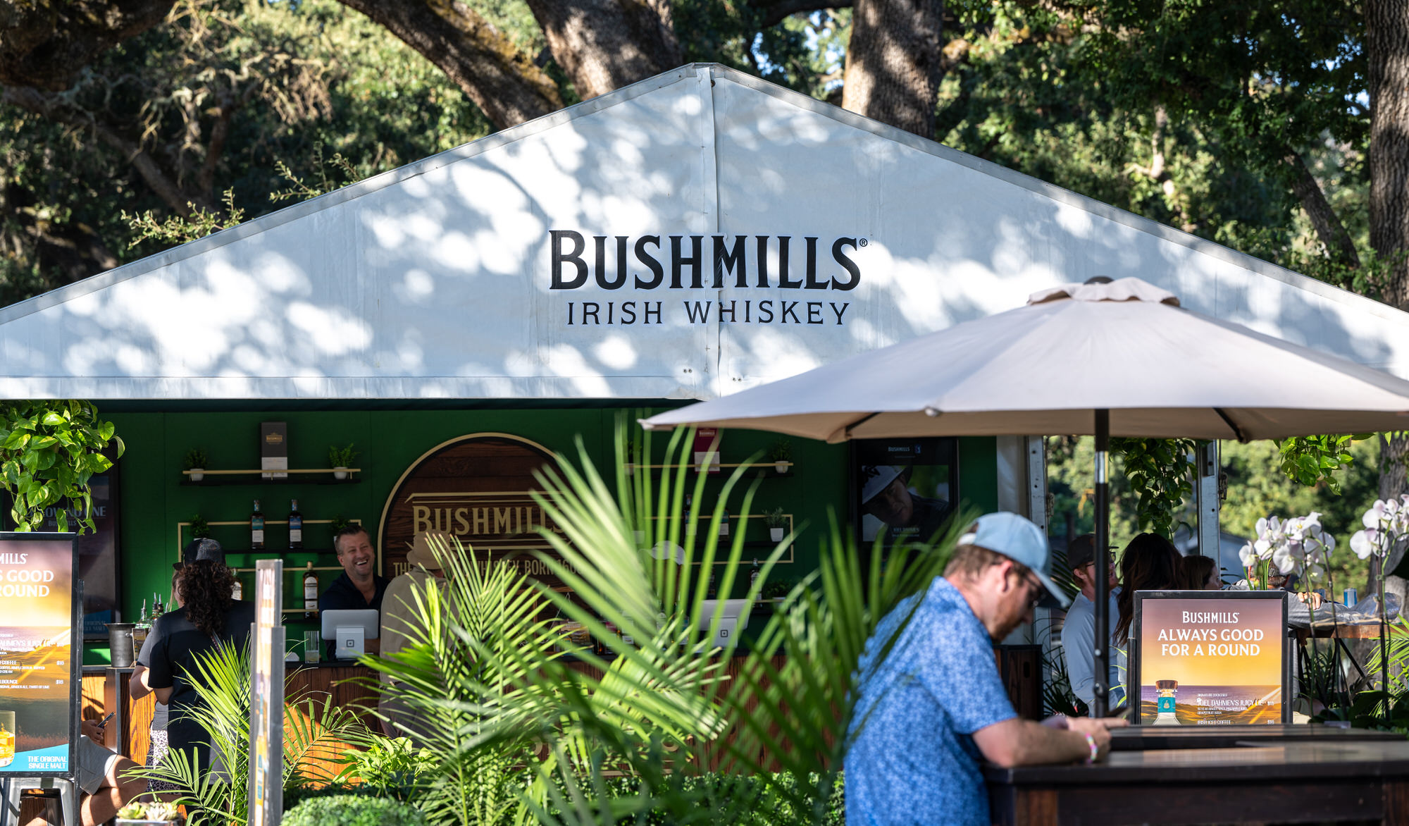 Guest ordering at a branded hospitality tent surrounded by palms