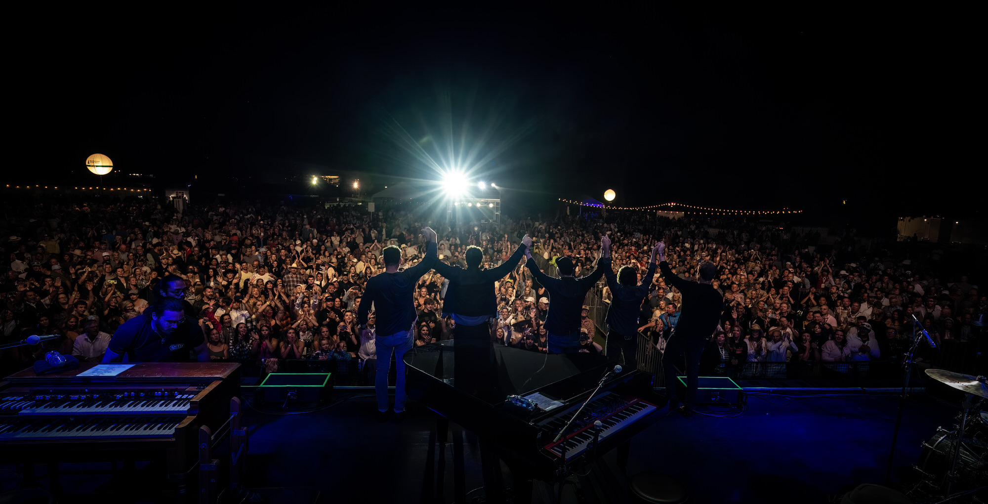 Band waving to a huge crowd from the front of the stage
