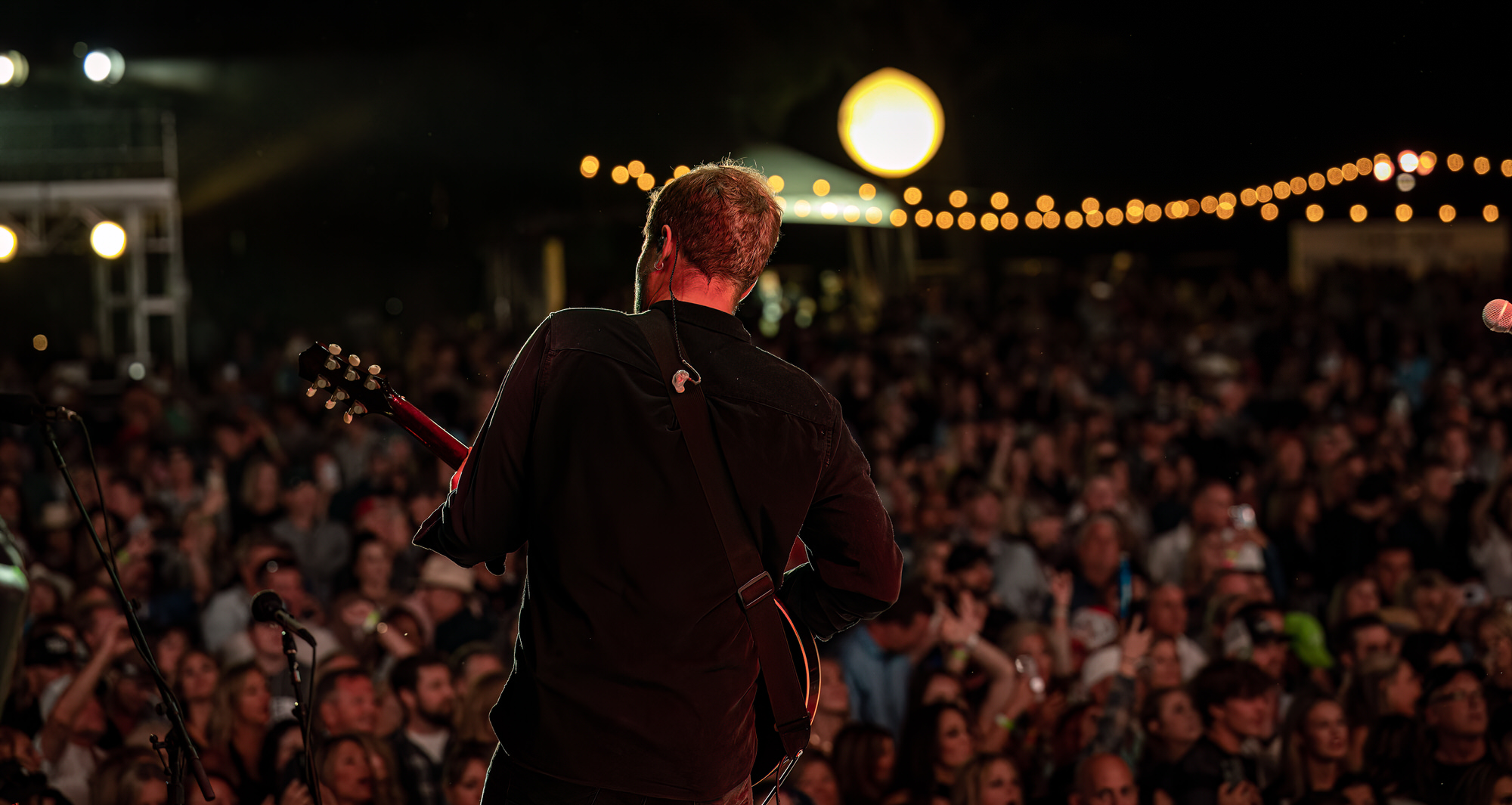 Guitarist facing a packed crowd under string lights
