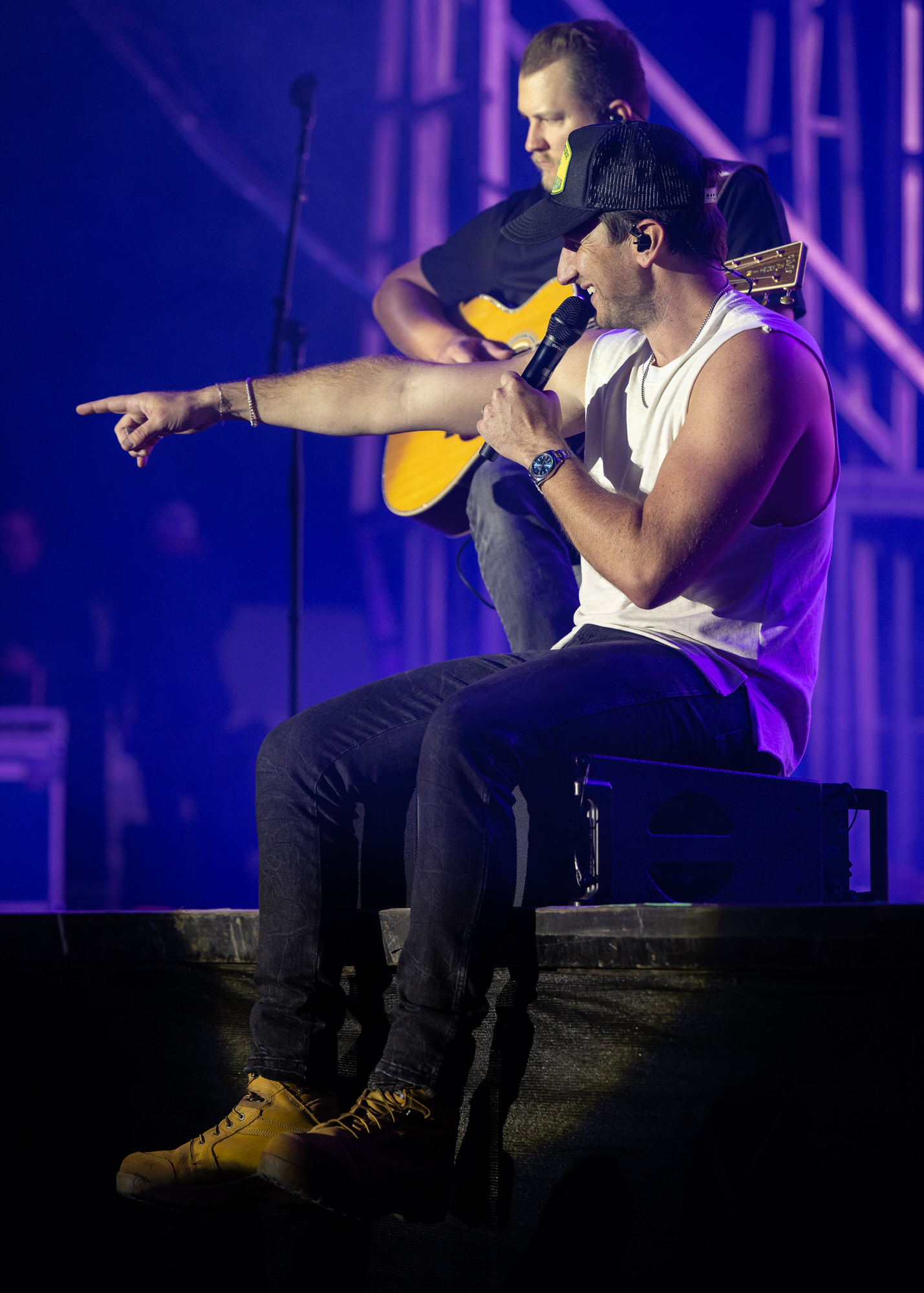 Seated singer pointing into the crowd while a guitarist plays behind him