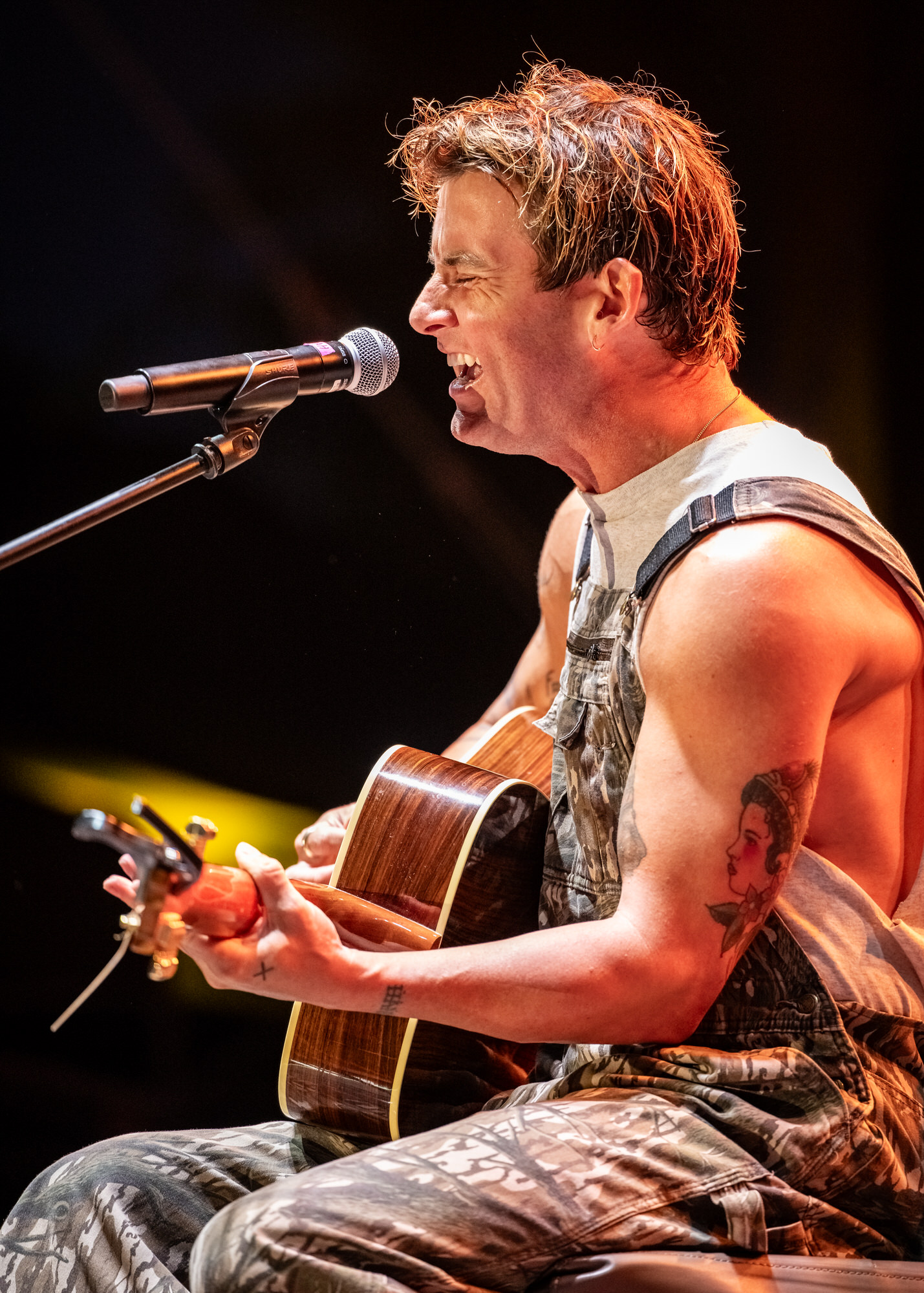 Seated singer playing acoustic guitar in warm stage light