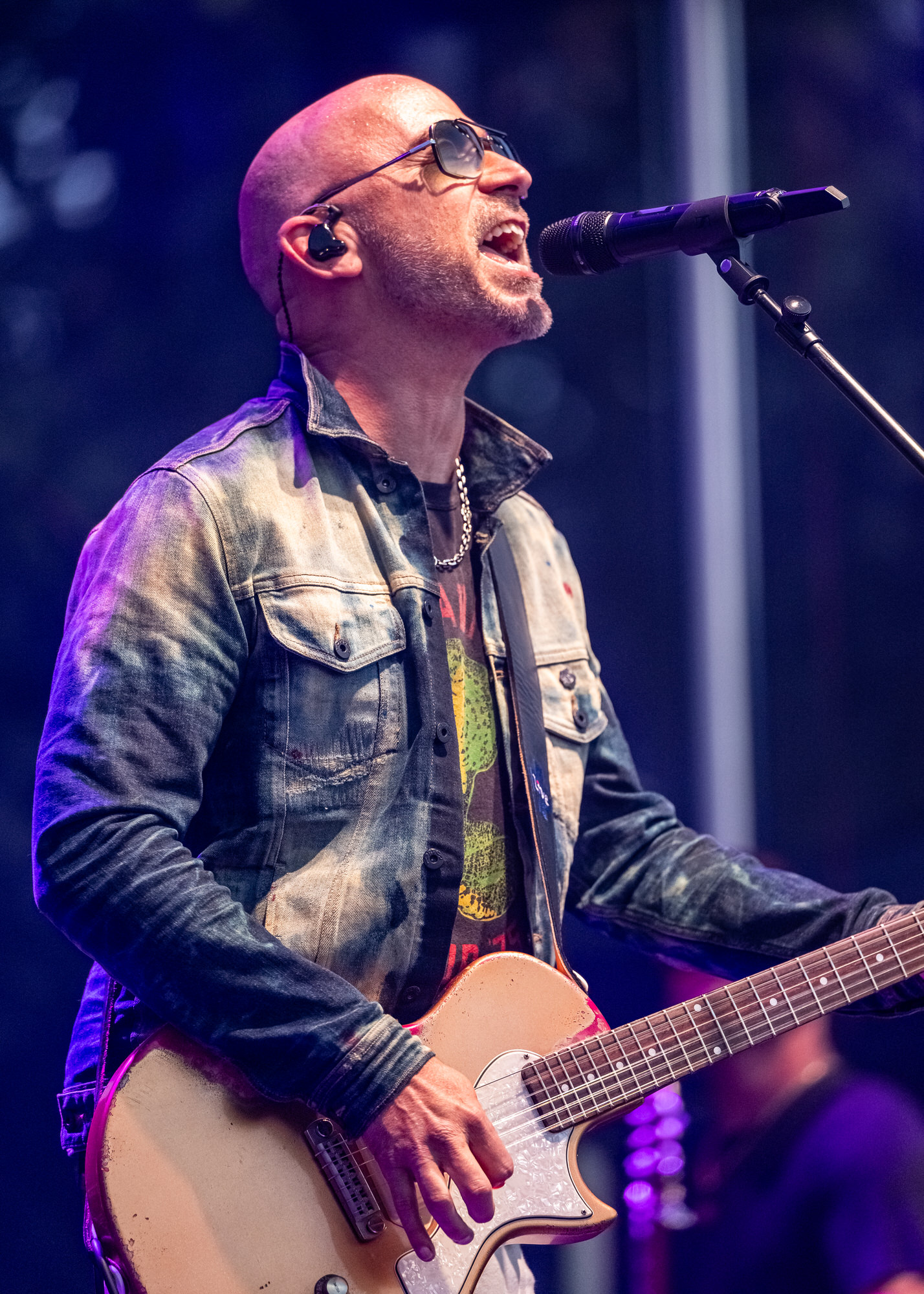 Singer in sunglasses playing electric guitar under blue stage light