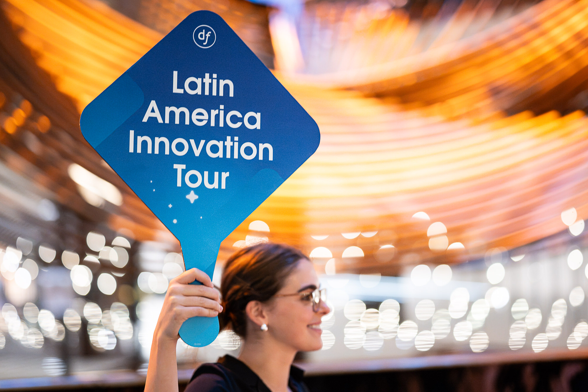 Smiling event host holding a paddle sign above a busy lobby