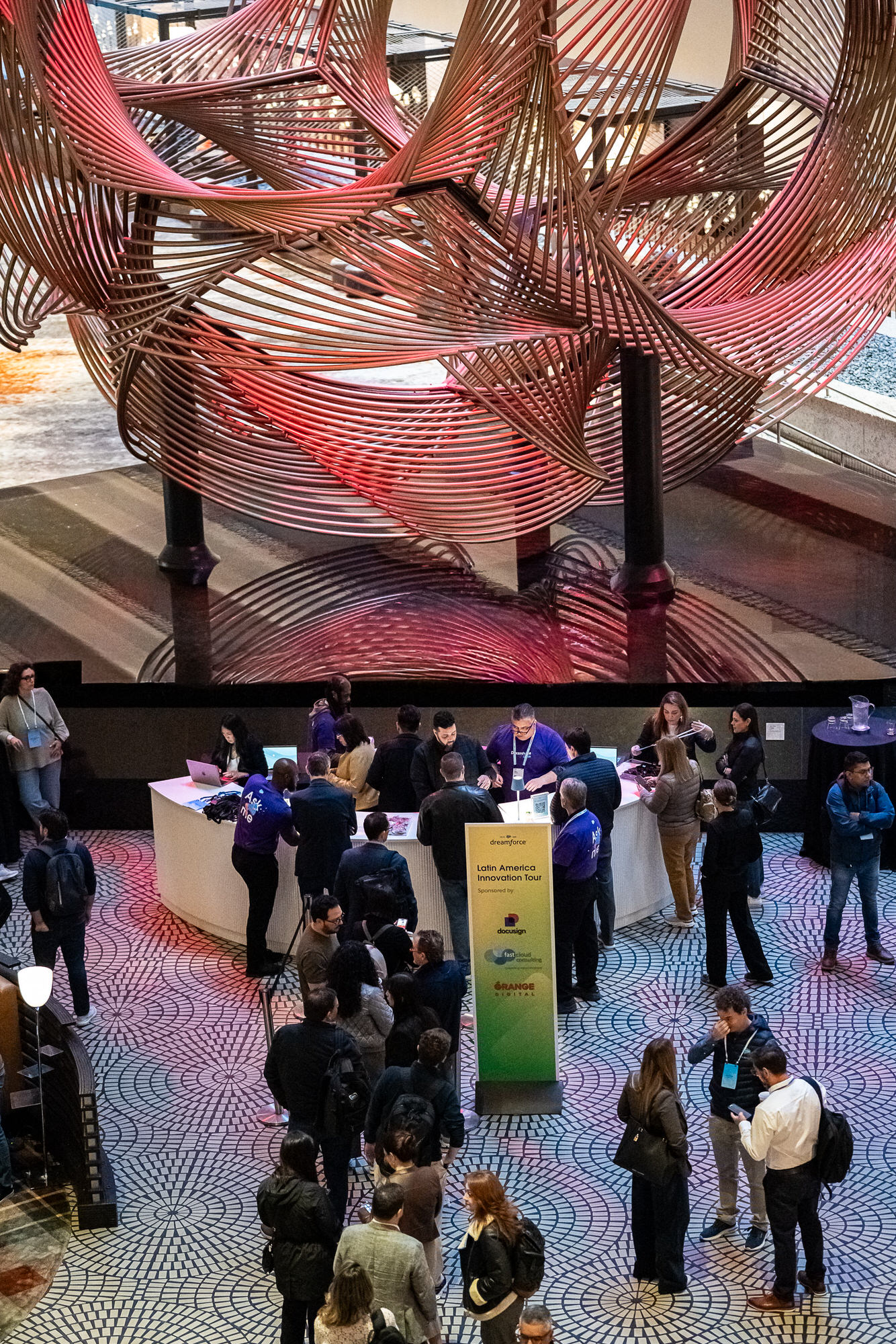Attendees gathering beneath a large red sculpture in a conference lobby, seen from above