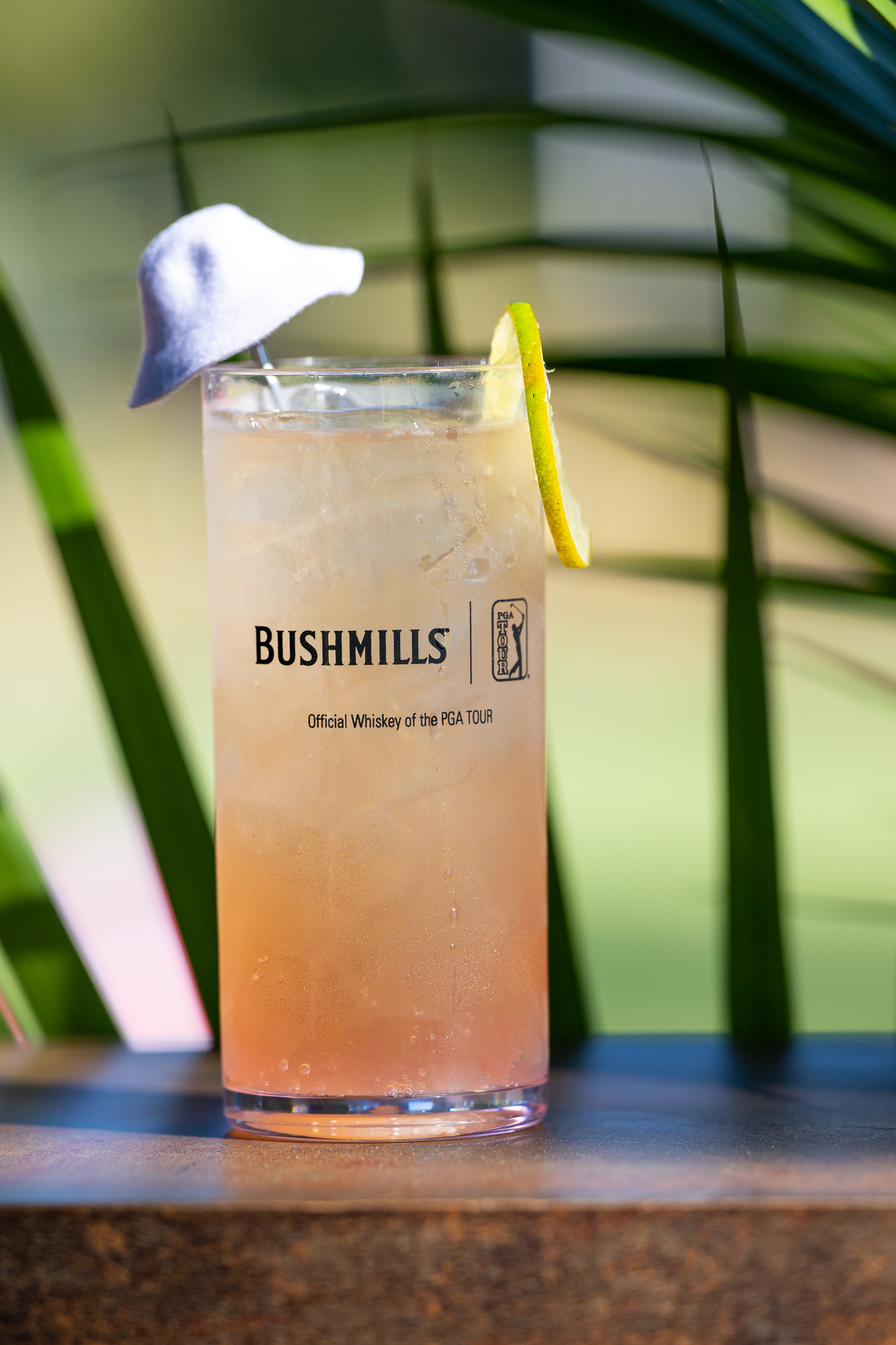 Signature cocktail in a branded glass, garnished with lime and a tiny bucket hat