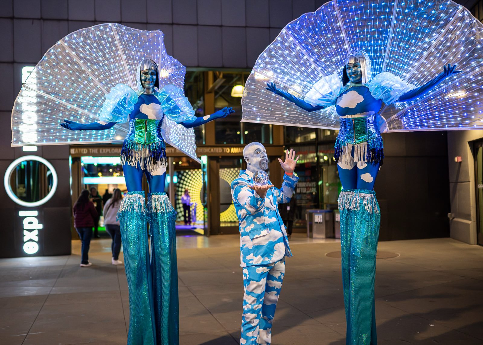 Stilt performers with lighted wings greeting guests at an evening reception