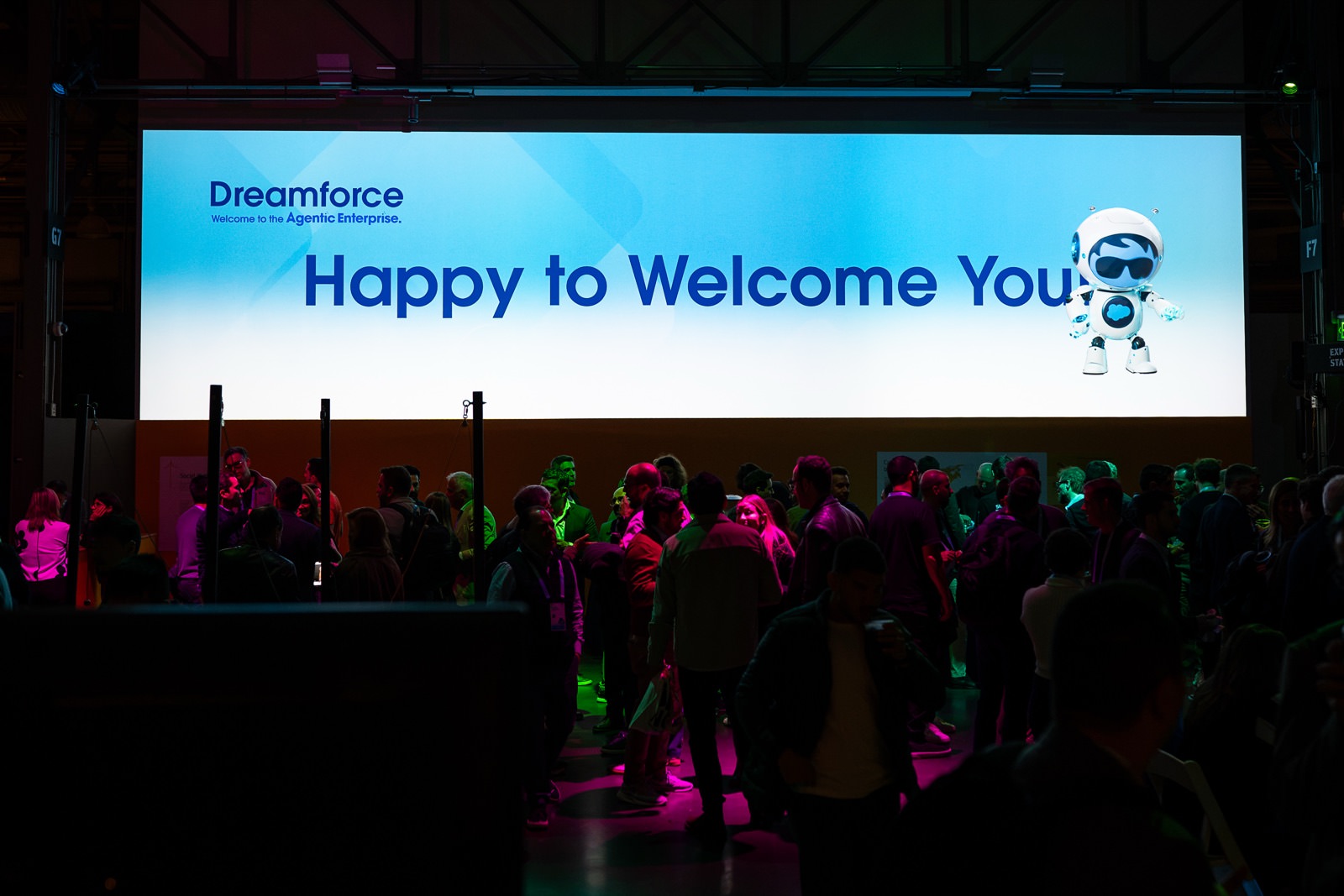 Welcome party crowd under colorful lights in front of the main screen
