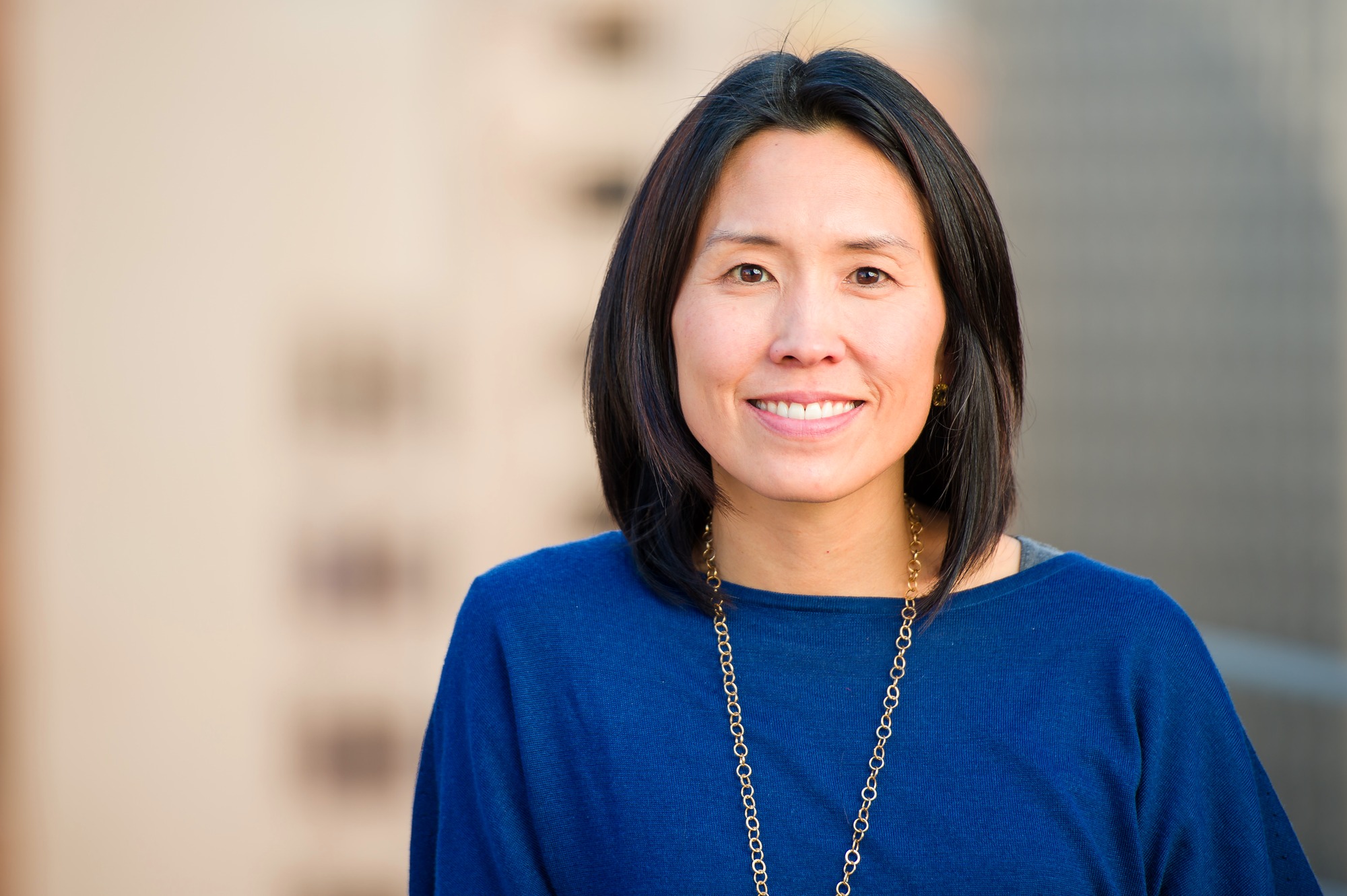 Corporate headshot of a woman in a navy top against a soft city backdrop