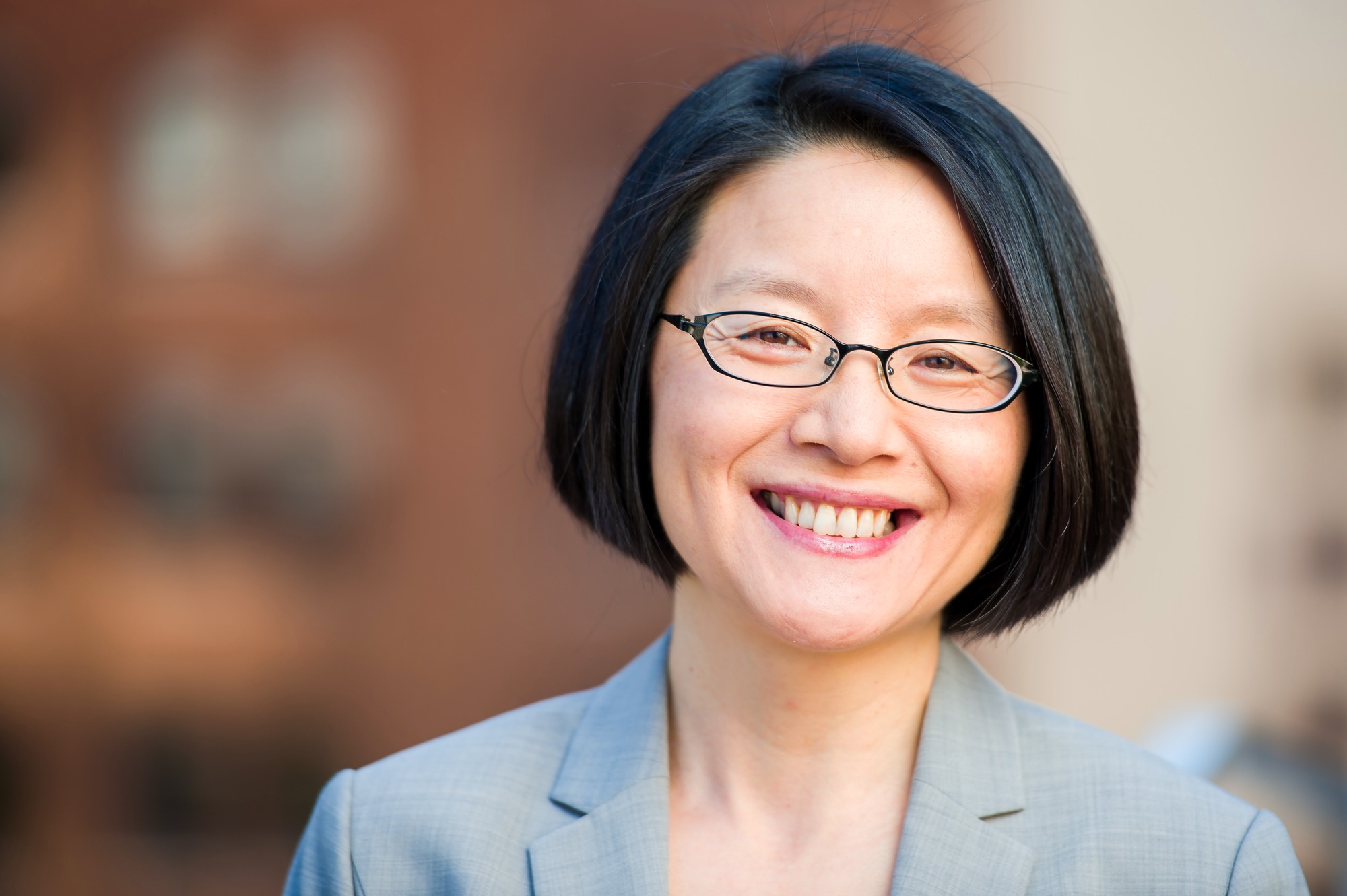 Corporate headshot of a woman with glasses in a gray blazer