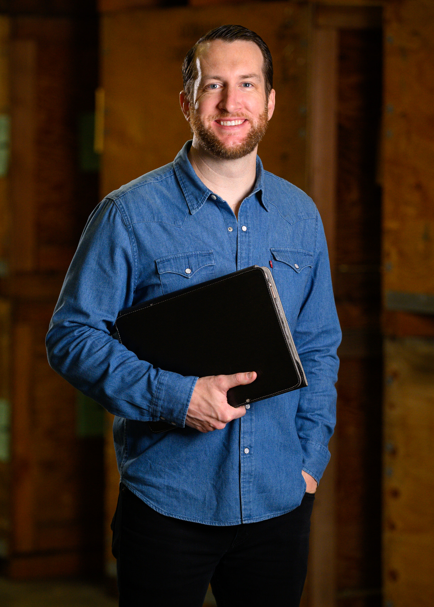 Portrait of a bearded man in a denim shirt holding a laptop